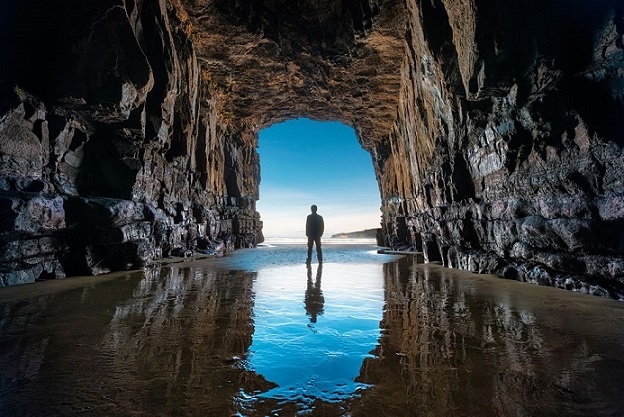 A picture from within a dark cave, showing a man standing at the entrance