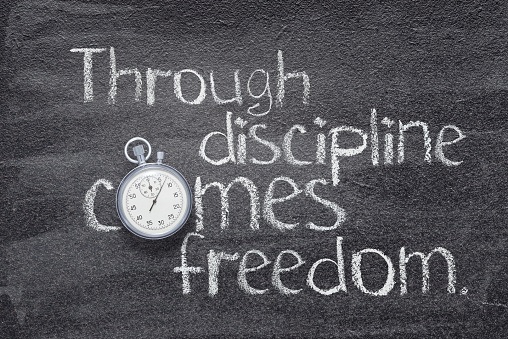 The words "through discipline comes freedom" written on a chalkboard. The "o" in the word "comes" is a round stopwatch.