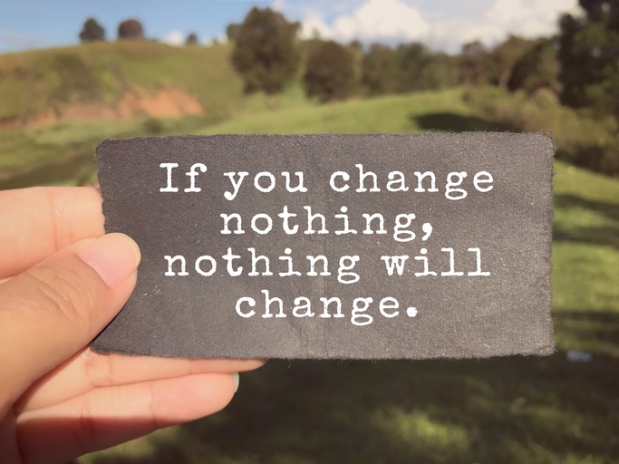 An outdoor background with grass and trees. A sign in the foreground that says "If you change nothing, nothing will change"