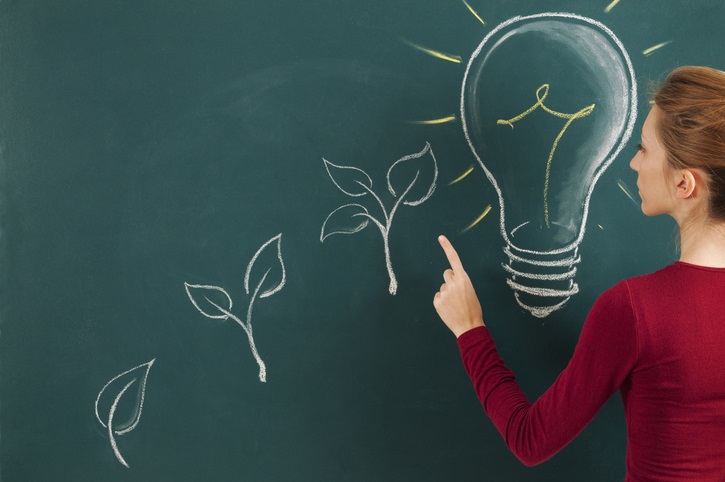 A person drawing at a chalkboard. The drawings are (from left to right, and in ascending order): a plant with 1 leaf, a plant with 2 leaves, a plant with 3 leavens, then finally a large light bulb