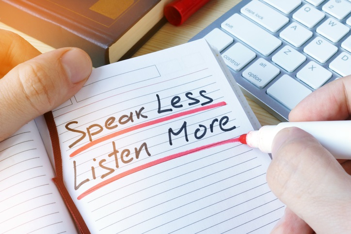 A notebook in which "speak less, listen more" is written in black ink and underlined in red ink