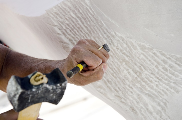 A large piece of white marble being sculpted with a hammer and chisel