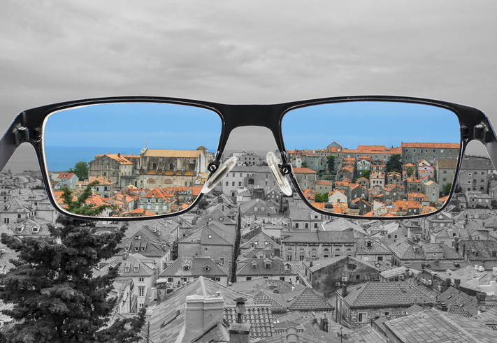 The view of a city through a pair of glasses with the background in gray and the view through the lenses of the glasses is in color