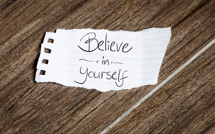 A brown background with a white piece of paper that says "believe in yourself"